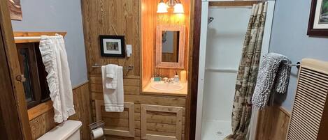 Un baño con paneles de madera, inodoro, lavabo con espejo y ducha.