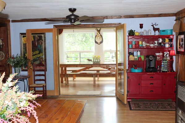 A room with wooden flooring, a dining table with benches, a red cabinet with various items, and a ceiling fan. - Bear Creek Guest Ranch (Essex)