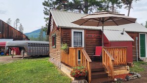 A rustic log cabin with a porch, a green door, and a sign reading "LEWIS & CLARK." - Bear Creek Guest Ranch (Essex)