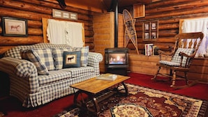A cozy log cabin interior with a plaid sofa, a rocking chair, a wooden coffee table, a fireplace, and a rustic wall decor. - Bear Creek Guest Ranch (Essex)