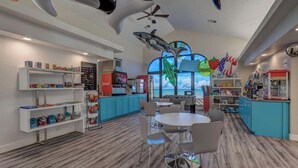 Zona de juegos infantiles con mesa de billar, asientos y vista al océano a través de amplios ventanales.