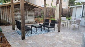 Un patio exterior con una pérgola de madera, una mesa de comedor con sillas y plantas en macetas.