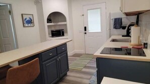 Una cocina compacta con microondas, un lavamanos y un pequeño comedor con una silla.