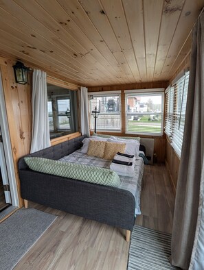 Interior de una cabaña de madera con cama, cortinas y vistas al exterior.