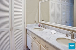 A bathroom with two sinks, a large mirror, and a set of louvered cabinets. - Isla Mazatlán Residence Club (Mazatlán)