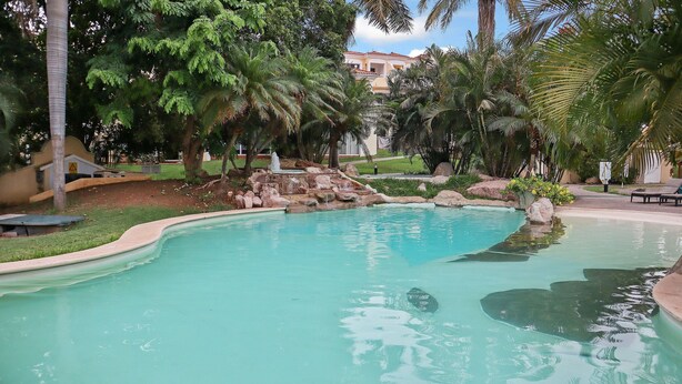 A swimming pool surrounded by palm trees and a stone waterfall. - Isla Mazatlán Residence Club (Mazatlán)