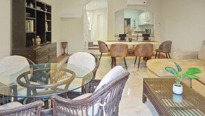 A spacious living room with a glass-top dining table surrounded by wicker chairs, a dark wooden bookshelf, and a beige sofa. - Isla Mazatlán Residence Club (Mazatlán)