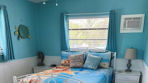 A bedroom with a bed, a nightstand, a window with curtains, a wall-mounted air conditioner, and a fish decoration.