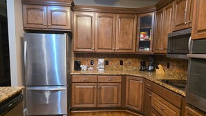 A kitchen with wooden cabinets, a stainless steel refrigerator, a microwave, and a granite countertop. - Large Private Home Near Charlotte Sleeps 15  Workspaces and Land - NO PETS (Dallas)