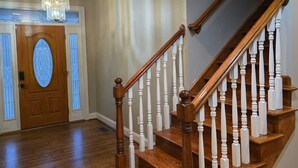 A wooden staircase with white balusters and a chandelier in a hallway with a wooden door and patterned glass panels. - Large Private Home Near Charlotte Sleeps 15  Workspaces and Land - NO PETS (Dallas)