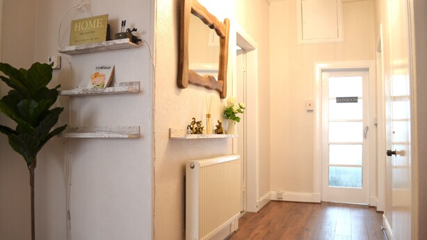 A hallway with a radiator, wooden shelves with decorative items, a mirror, and a door labeled "BATHROOM". - Charming Spacious Central Apartment (Edinburgh)