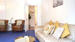 A living room with a blue carpet, two leather armchairs, a patterned sofa, and a round coffee table. - Charming Spacious Central Apartment (Edinburgh)