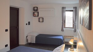 A small, single-bed room with a window, a radiator, a door, and a wall-mounted air conditioner. - B & B Family in the heart of the Village of Aieta (Cs) (Aieta)