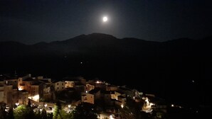 A nighttime view of a town with buildings illuminated by streetlights, a visible moon, and mountains in the background. - B & B Family in the heart of the Village of Aieta (Cs) (Aieta)