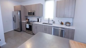 Une cuisine moderne dotée d’appareils électroménagers en acier inoxydable, de meubles de rangement en bois clair et d’une grande fenêtre qui laisse entrer la lumière naturelle.