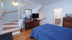 Une chambre à coucher avec un lit, une commode, un téléviseur et un escalier.