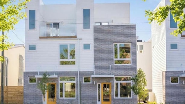 Un immeuble résidentiel moderne à plusieurs étages, doté d’un toit plat, de grandes fenêtres et d’un revêtement extérieur combinant des couleurs blanche et grise.
