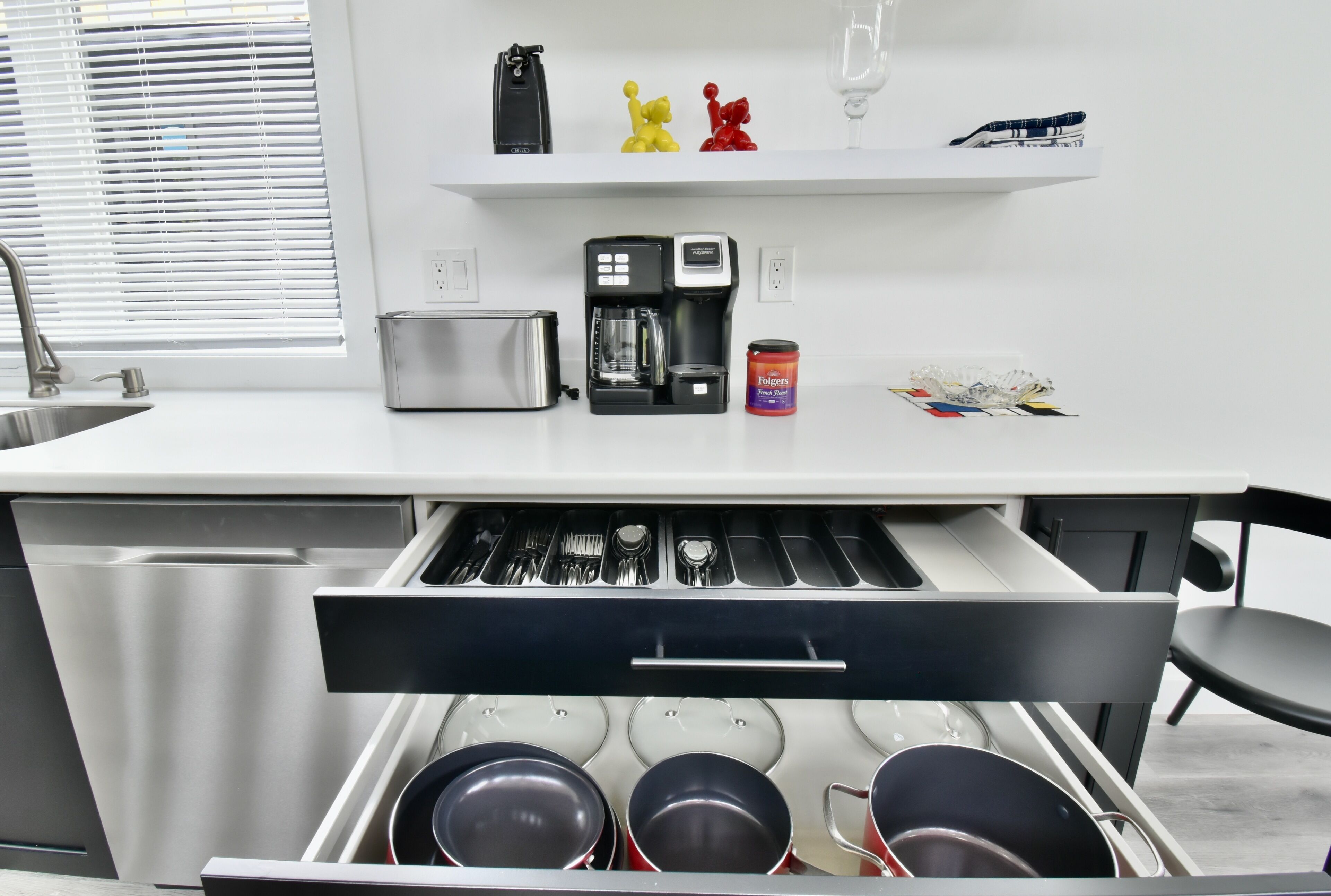 Uma cozinha moderna com torradeira embutida, máquina de café e uma gaveta com panelas.