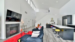 Un salon moderne avec une cheminée, un grand canapé, un tapis rouge et un téléviseur fixé au mur.