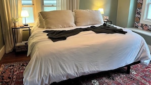 A neatly made bed with two pillows, a bedside table with a lamp, and a window with curtains. - The Portage Place: 3BR 2 mi from ND w/ king suite (South Bend)