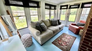 A sunroom with a light blue floor, a beige sofa with patterned cushions, a red chair, and a patterned rug. - The Portage Place: 3BR 2 mi from ND w/ king suite (South Bend)