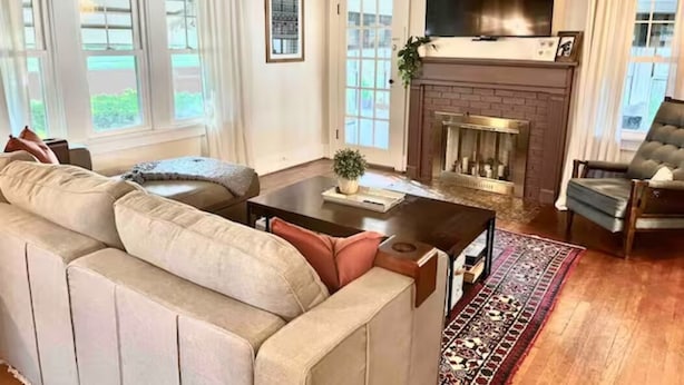 A living room with a beige sofa, a coffee table, a fireplace, and a television mounted above it. - The Portage Place: 3BR 2 mi from ND w/ king suite (South Bend)