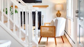 Una escalera con balaustres blancos, una silla de mimbre, una lámpara y un televisor fijado en la pared.