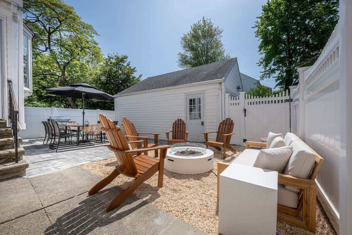 A backyard with a fire pit, wooden chairs, a white sofa, and a dining area with outdoor furniture.