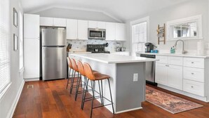 A modern kitchen with white cabinetry, stainless steel appliances, and a central island with bar stools.