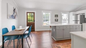 A modern kitchen with grey cabinets, a wooden dining table with blue chairs, and a large window.