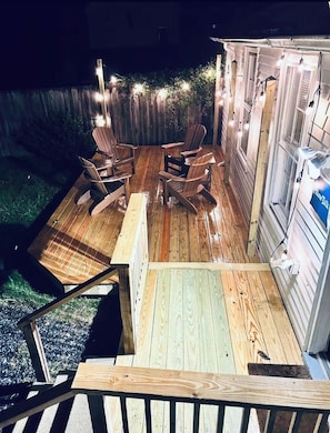 Puisesta laudasta rakennettu terassi, jossa on Adirondack-tyyliset tuolit, pieni pöytä ja koristeelliset valonauhat.