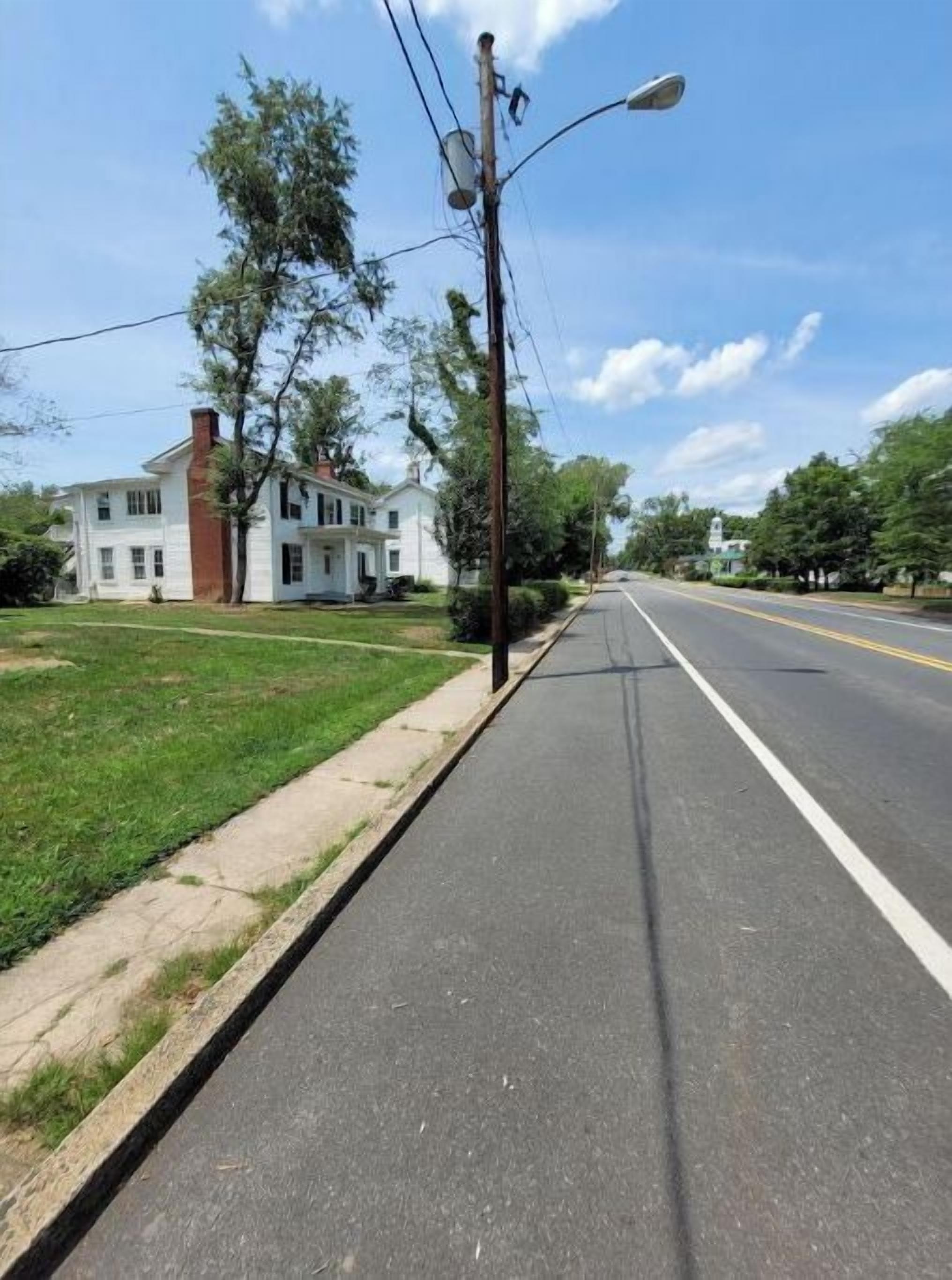 A two-story white house with a red brick chimney, a paved sidewalk, and a street with a bike lane.