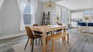 A modern kitchen with white cabinets, a wooden dining table, and a bar area with blue bar stools. - Steps to Park Circle! | The Cavalier (North Charleston)