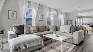 A modern living room with a sectional sofa, a coffee table, and a kitchen in the background. - Steps to Park Circle! | The Cavalier (North Charleston)