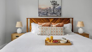 A neatly made bed with a tray of breakfast items, two bedside lamps, and a desert landscape painting on the wall. - Steps to Park Circle! | The Cavalier (North Charleston)