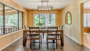 Ein Essbereich mit Holztisch und -stühlen, großen Fenstern und einer Deckenleuchte.