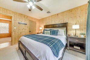 Une chambre avec un mur lambrissé en bois, un lit recouvert d’une couette bleue et blanche, une table de chevet avec une lampe et un ventilateur de plafond.