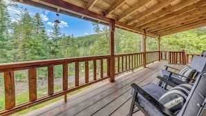 Eine Holzdielen-Terrasse mit Geländer, Sitzgelegenheiten im Freien und Blick auf einen Wald.