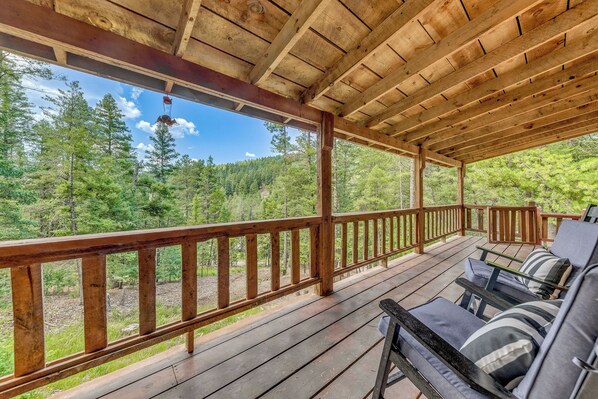 Une terrasse en bois avec une rambarde, des sièges d’extérieur et une vue sur une forêt.