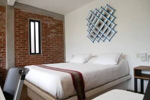 A bedroom with a brick wall, a window, a bed with white bedding, and a decorative wall piece. - Las Orquídeas A, Casa con vista al Tepozteco (Tepoztlán)