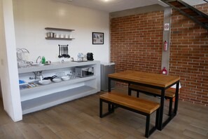 A compact kitchen with white cabinets, a microwave, a coffee maker, and a brick wall. - Las Orquídeas A, Casa con vista al Tepozteco (Tepoztlán)