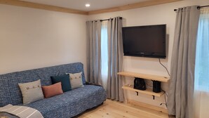 Ein Wohnzimmer mit einem blauen Sofa, einem Flachbildfernseher an der Wand und einem Holzregal darunter.