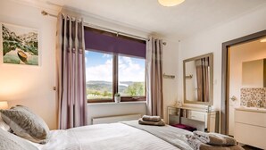 Une chambre avec un grand lit, une fenêtre donnant sur les montagnes, une table de chevet avec une lampe et une commode avec un miroir.