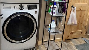 A laundry area with a stacked washer and dryer, a metal shelf with cleaning supplies, and a wooden door.