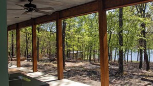 A covered outdoor area with wooden beams and a table, overlooking a forested area with a lake.