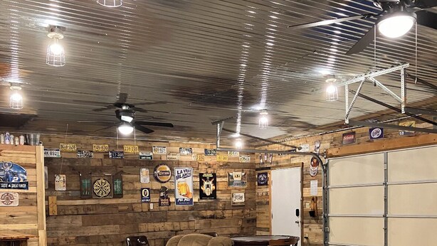 Un intérieur rustique avec un mur en bois, un canapé gris, une table en bois et un ventilateur de plafond.