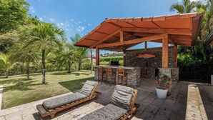 Een terras met twee lounge fauteuils, een barbecueplaats met stenen en een plant in pot.