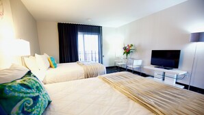 Ein Hotelzimmer mit zwei Betten, einem Flachbildfernseher, einem Schreibtisch mit Stuhl und einem großen Fenster mit Vorhängen.