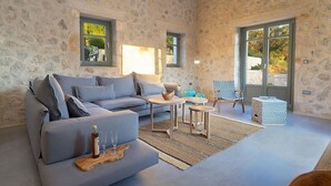 Una sala de estar acogedora con un sofá gris, dos mesitas pequeñas, una mesa de centro de madera y un reposapiés estampado.