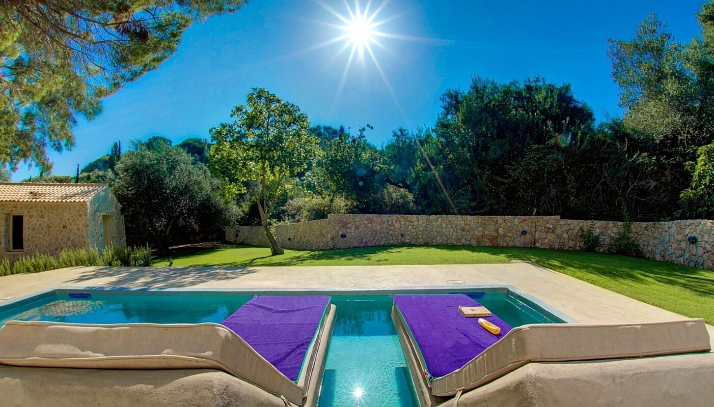 A swimming pool with two lounge chairs, a stone wall, and a clear blue sky.